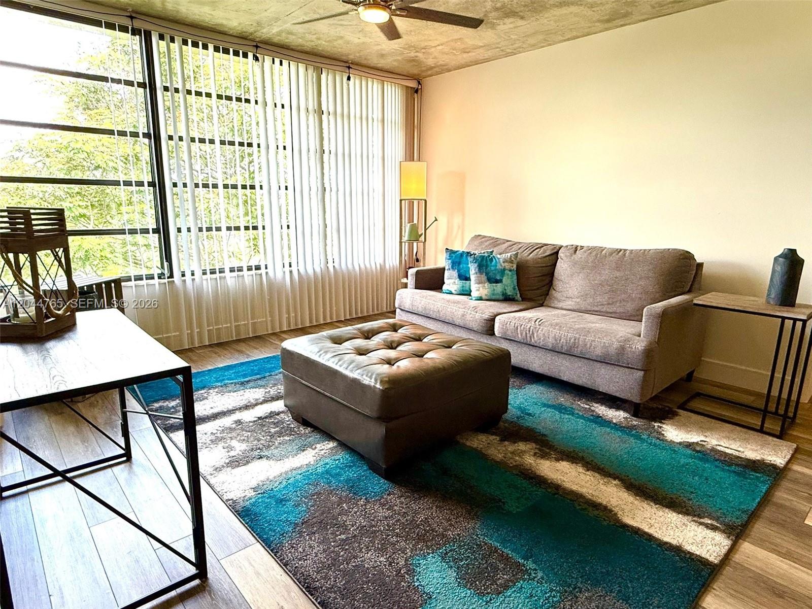 A living room features a grey sofa, a tufted ottoman, and a blue patterned rug — 1705 Whitehall Dr # 403, Davie FL 33324, DAVIE, FL