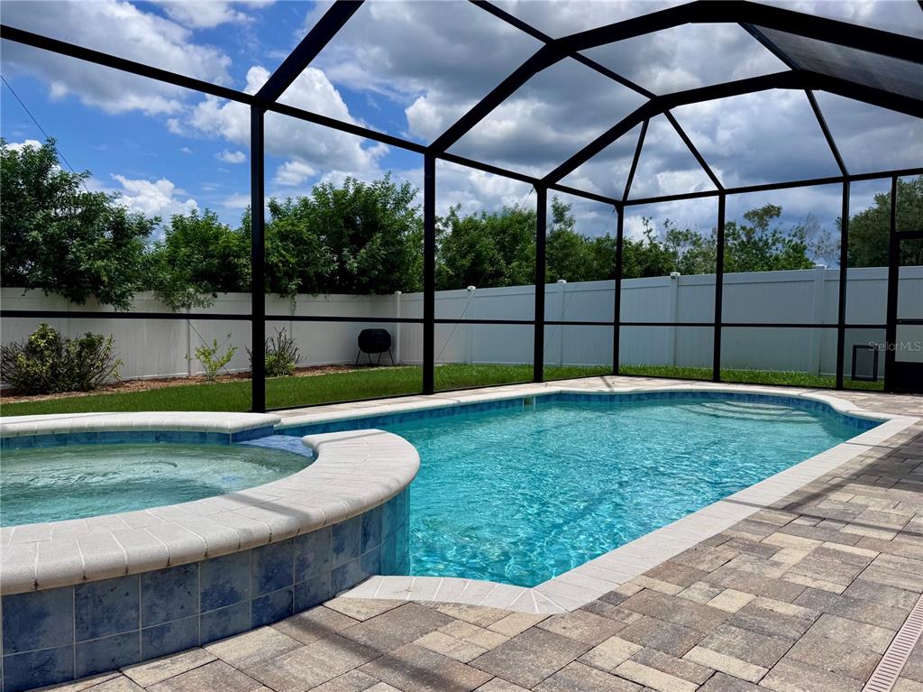 A swimming pool and spa enclosed by a screened lanai with a white privacy fence — 1625 EMERALD HILL WAY, VALRICO, FL