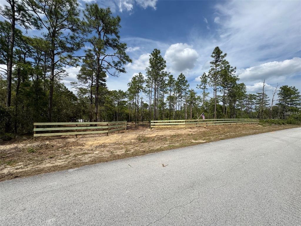 A wooden fence borders a vacant, wooded lot along a paved road — SW EDGEWATER BOULEVARD, DUNNELLON, FL