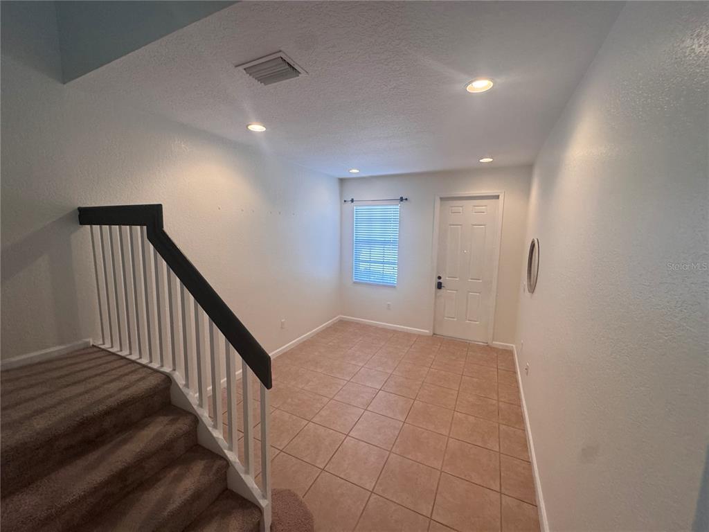 An entryway features a carpeted staircase with a black railing and light-colored tile flooring — 3469 ALLEGRA CIRCLE, ST CLOUD, FL