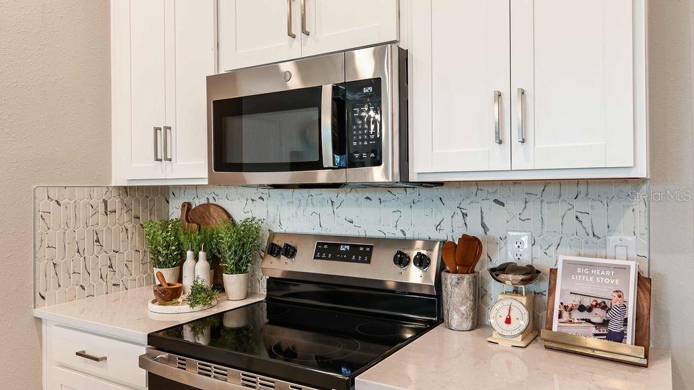 A kitchen features white cabinets, a stainless steel microwave, a glass-top stove, and marble-patterned backsplash — 42 ARMOYAN DRIVE, PALM COAST, FL