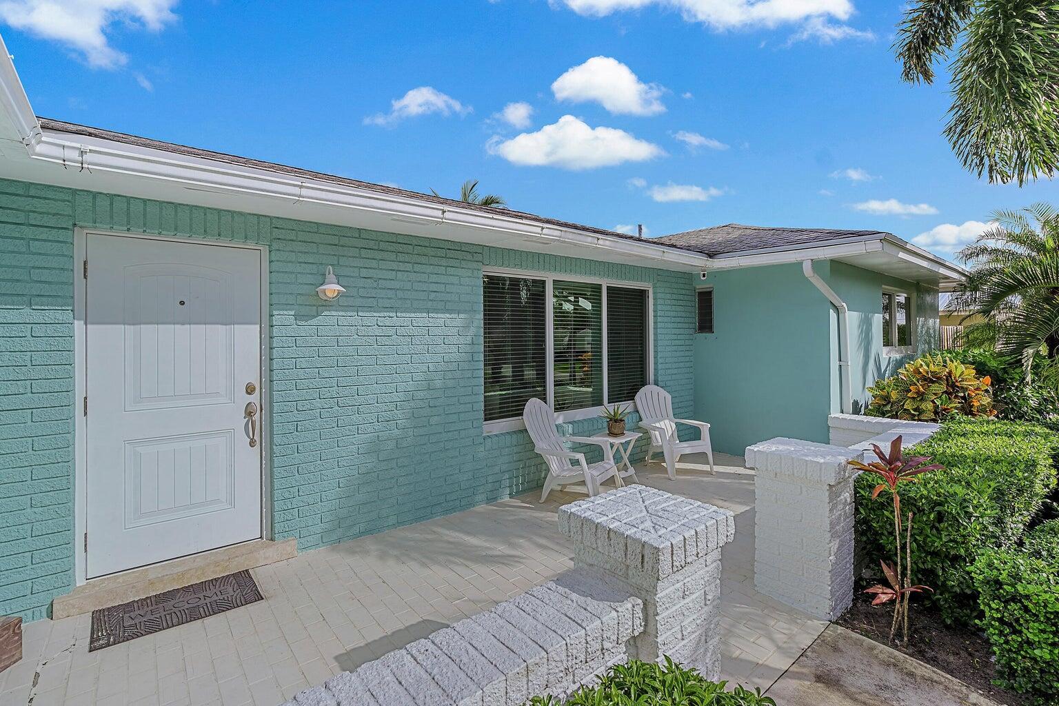 A light blue brick house features a white front door and a small paved patio — 356 Mars Avenue, Tequesta FL 33469, TEQUESTA, FL