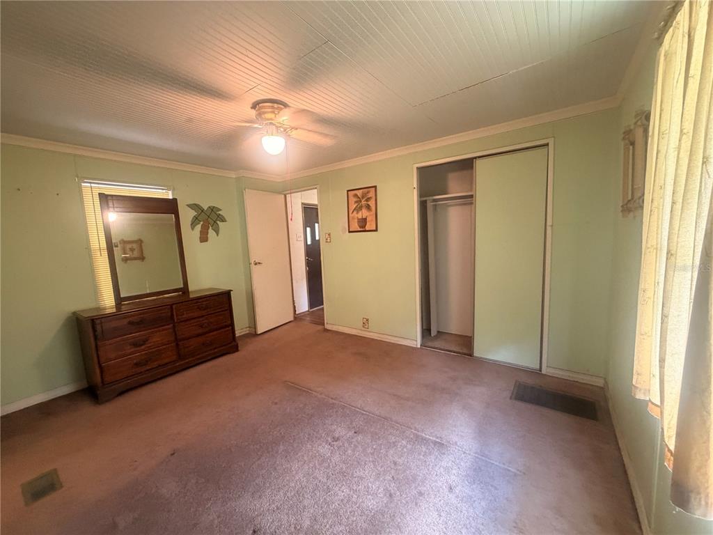 A bedroom with light green walls, tan carpet, a wooden dresser, and a sliding closet door — 8582 W ADMIRAL BYRD LANE, CRYSTAL RIVER, FL