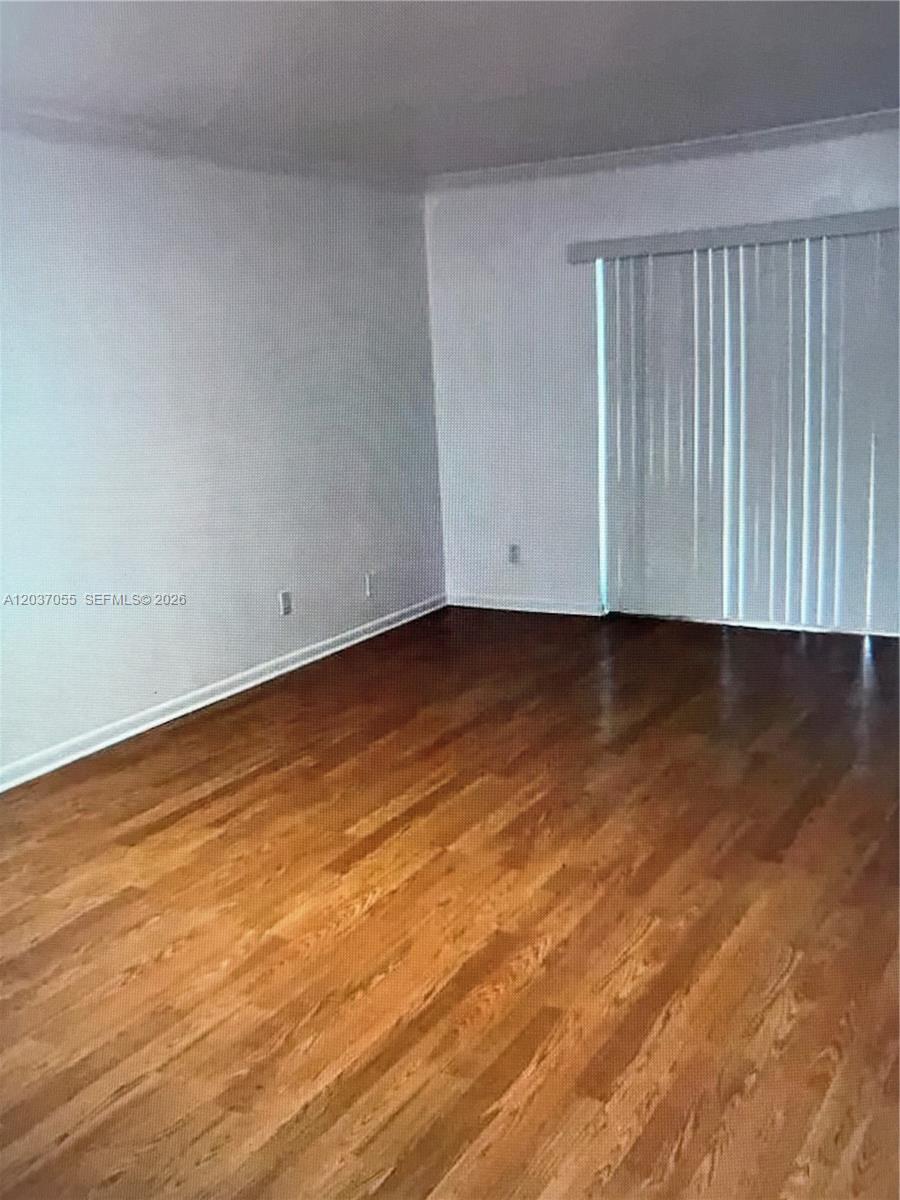 An empty room features hardwood flooring, white walls, and vertical blinds covering a sliding door — 17000 NW 67th Ave # 445, Hialeah FL 33015, HIALEAH, FL