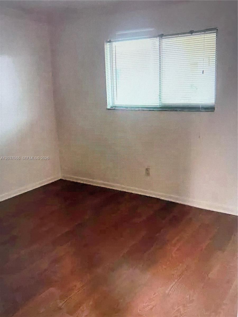 An empty bedroom features dark wood-look flooring and a single window with white blinds — 17000 NW 67th Ave # 445, Hialeah FL 33015, HIALEAH, FL