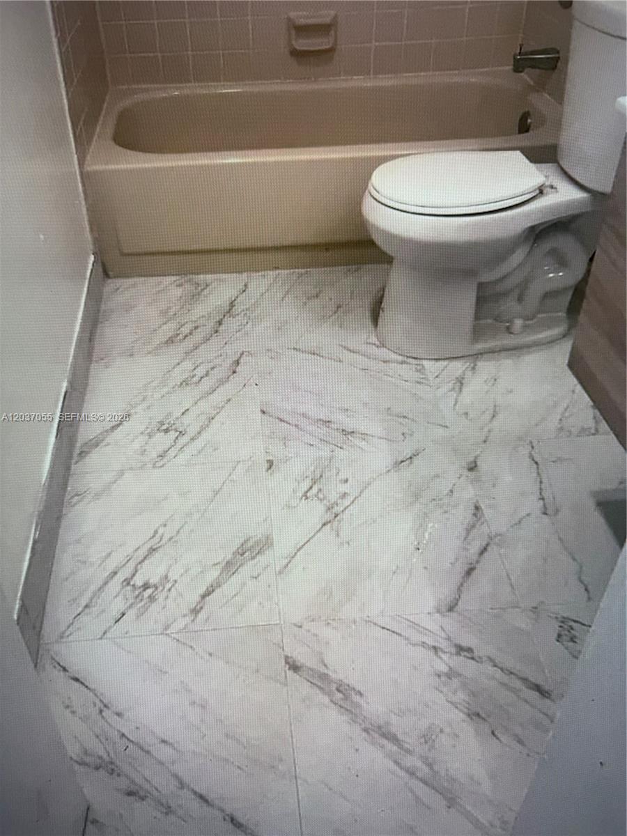 A bathroom features a beige bathtub, a white toilet, and light-colored marble-patterned floor tiles — 17000 NW 67th Ave # 445, Hialeah FL 33015, HIALEAH, FL