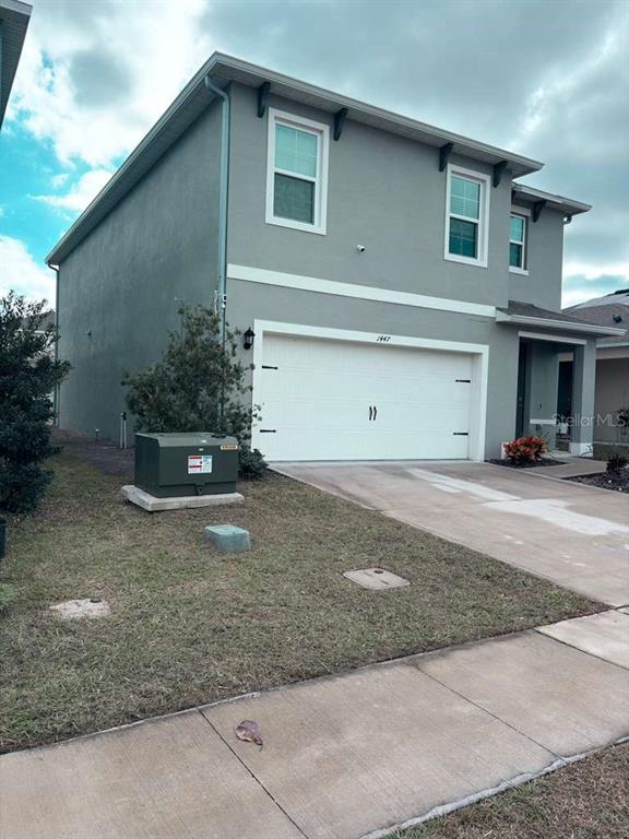 A two-story gray house features a white garage door and a concrete driveway — 1447 BERRY LANE, DAVENPORT, FL