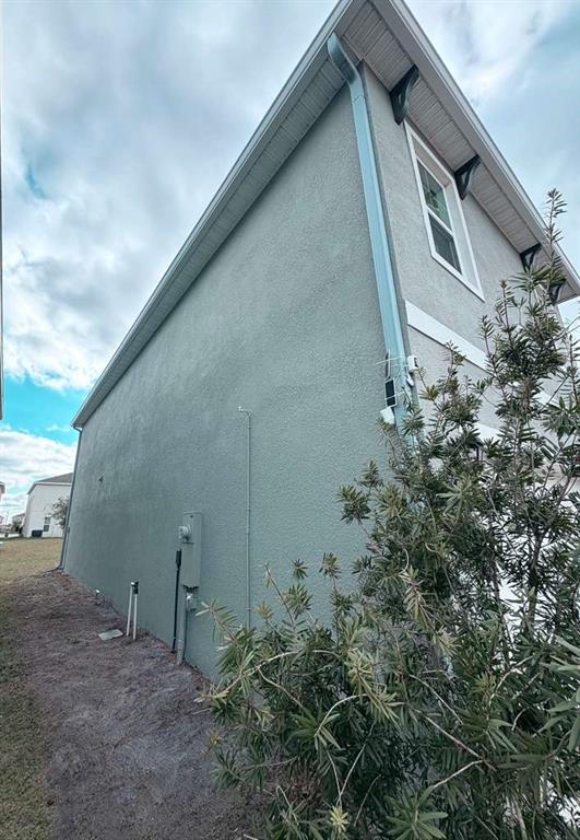 The side exterior of a two-story house features gray stucco siding, a downspout, and landscaping — 1447 BERRY LANE, DAVENPORT, FL
