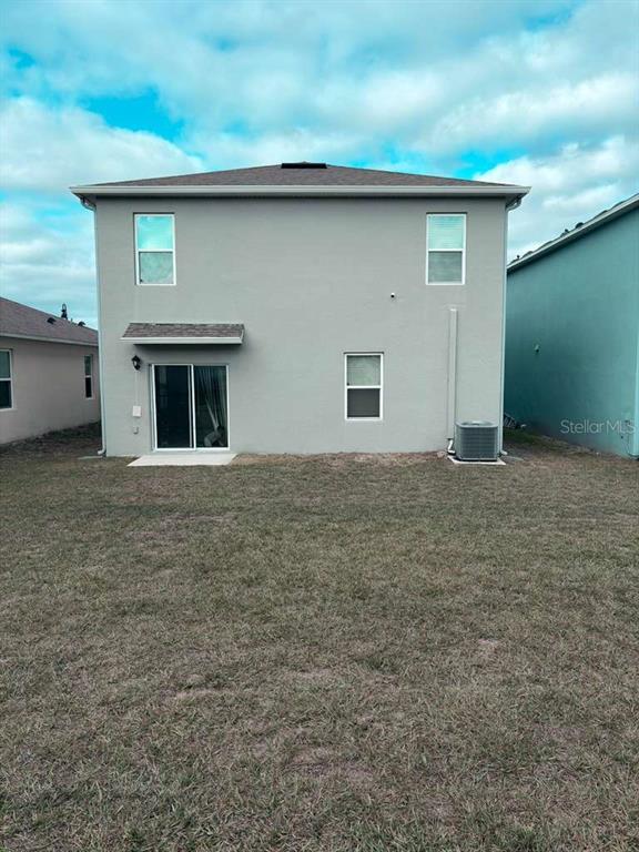 The rear exterior of a two-story gray stucco house features a sliding glass door and yard — 1447 BERRY LANE, DAVENPORT, FL