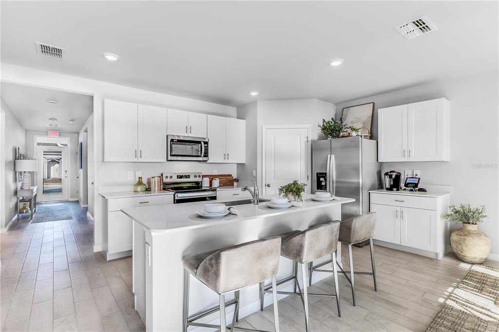 A modern kitchen features white cabinetry, a central island with bar seating, and stainless appliances — 4948 TUSCOLA BOULEVARD, NORTH PORT, FL