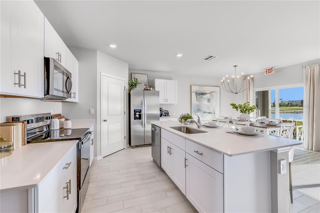 A modern kitchen features white cabinetry, quartz countertops, a large island, and stainless steel appliances — 4948 TUSCOLA BOULEVARD, NORTH PORT, FL