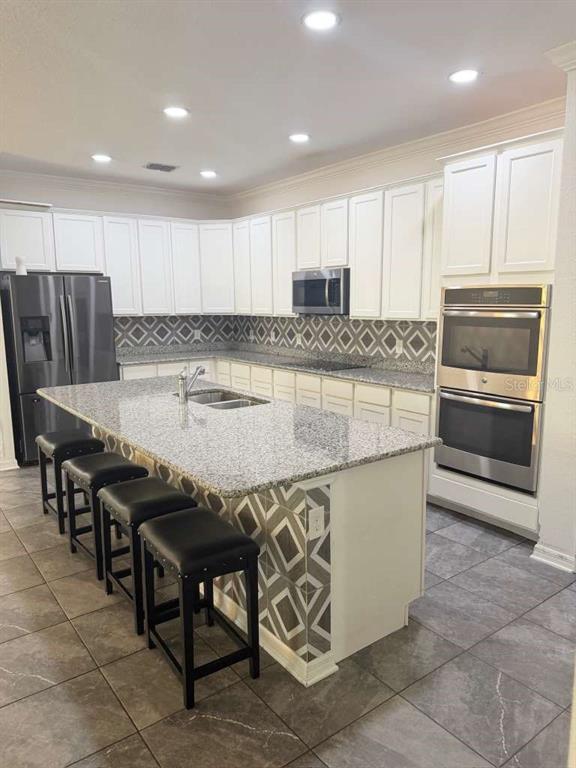 A kitchen features white cabinetry, granite countertops, a large island with seating, and patterned tile — 14305 FISSORE BOULEVARD, WIMAUMA, FL