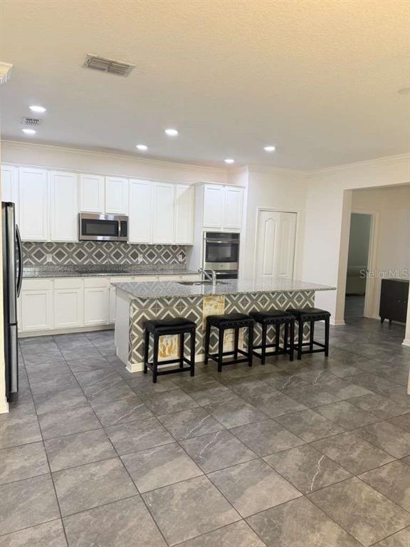 A kitchen features white cabinets, granite countertops, a patterned backsplash, and a central island — 14305 FISSORE BOULEVARD, WIMAUMA, FL