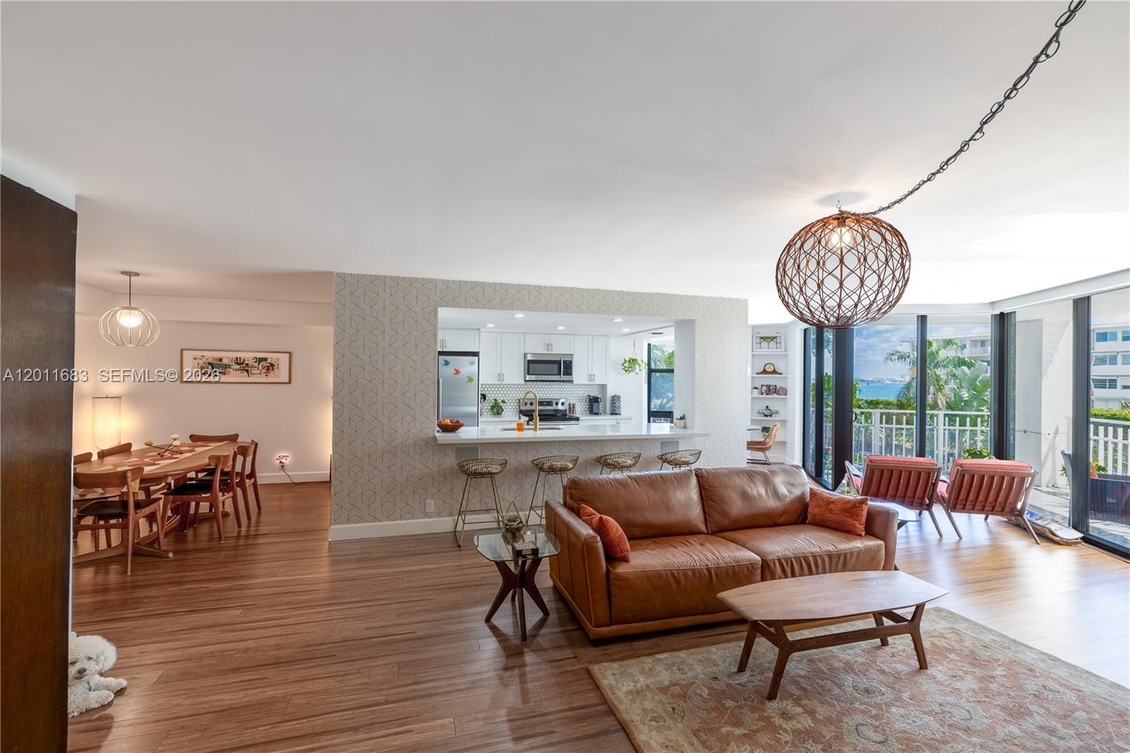 An open-concept living and dining area features a leather sofa, kitchen island, and balcony view — 4000 Towerside Ter # 308, Miami FL 33138, MIAMI, FL