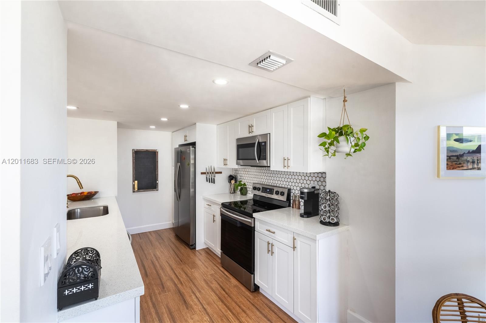 A modern kitchen features white cabinets, stainless steel appliances, and a hexagonal tile backsplash — 4000 Towerside Ter # 308, Miami FL 33138, MIAMI, FL