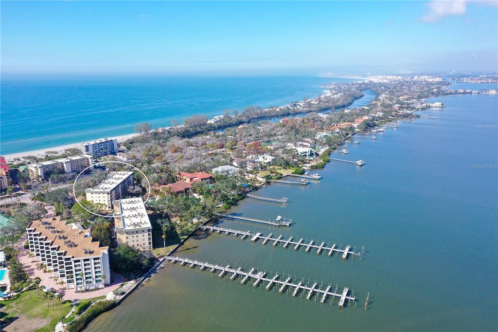 An aerial view shows a coastal apartment complex with a marina on the water — 8625 MIDNIGHT PASS ROAD UNIT 305B, SARASOTA, FL