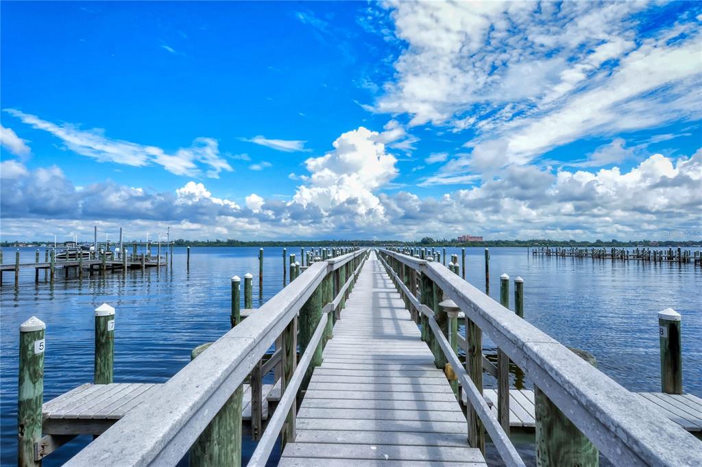 A wooden pier extends over calm water toward a distant shoreline under a cloudy sky — 8625 MIDNIGHT PASS ROAD UNIT 305B, SARASOTA, FL