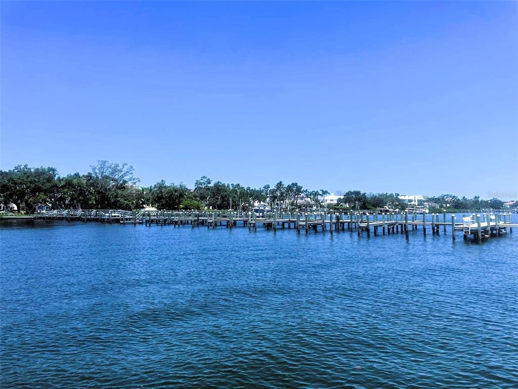 A long wooden dock extends into a calm body of water toward a treelined shore — 8625 MIDNIGHT PASS ROAD UNIT 305B, SARASOTA, FL