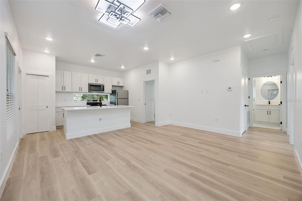 A bright open-concept kitchen and living area featuring white cabinetry, an island, and wood flooring — 521 W HERRIOTT AVENUE, OAKLAND, FL