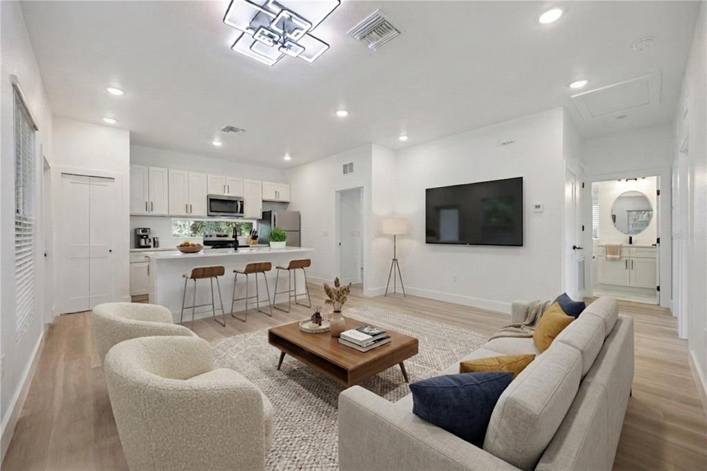 An open-concept living room and kitchen featuring light wood floors, white cabinetry, and modern furniture — 521 W HERRIOTT AVENUE, OAKLAND, FL
