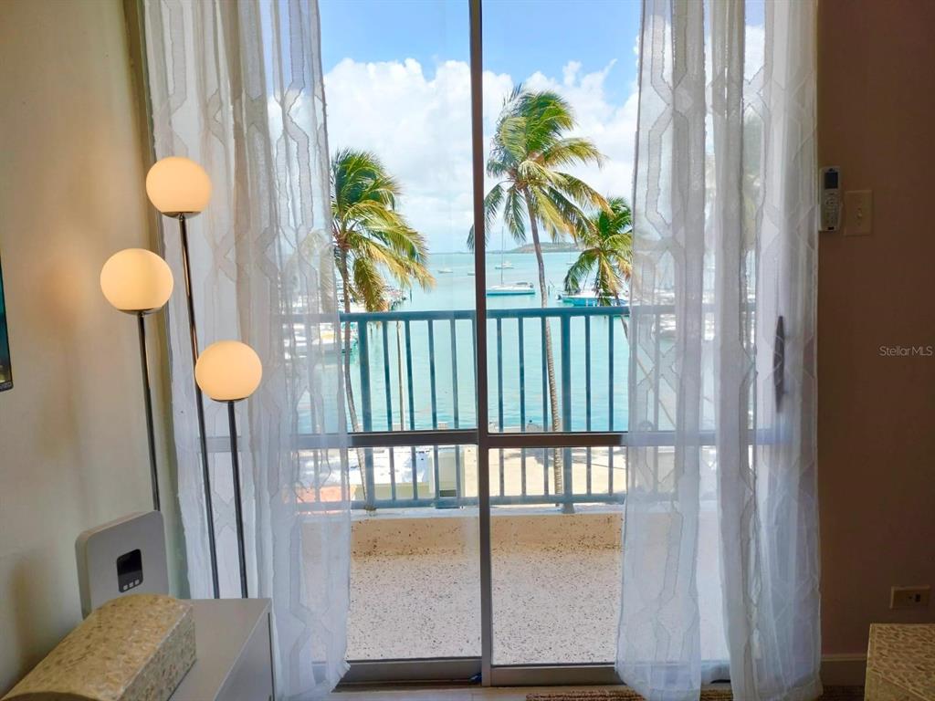 A view of a tropical harbor through a sliding glass door with sheer white curtains — Tower 1 ISLETA MARINA UNIT 4C, FAJARDO, PR