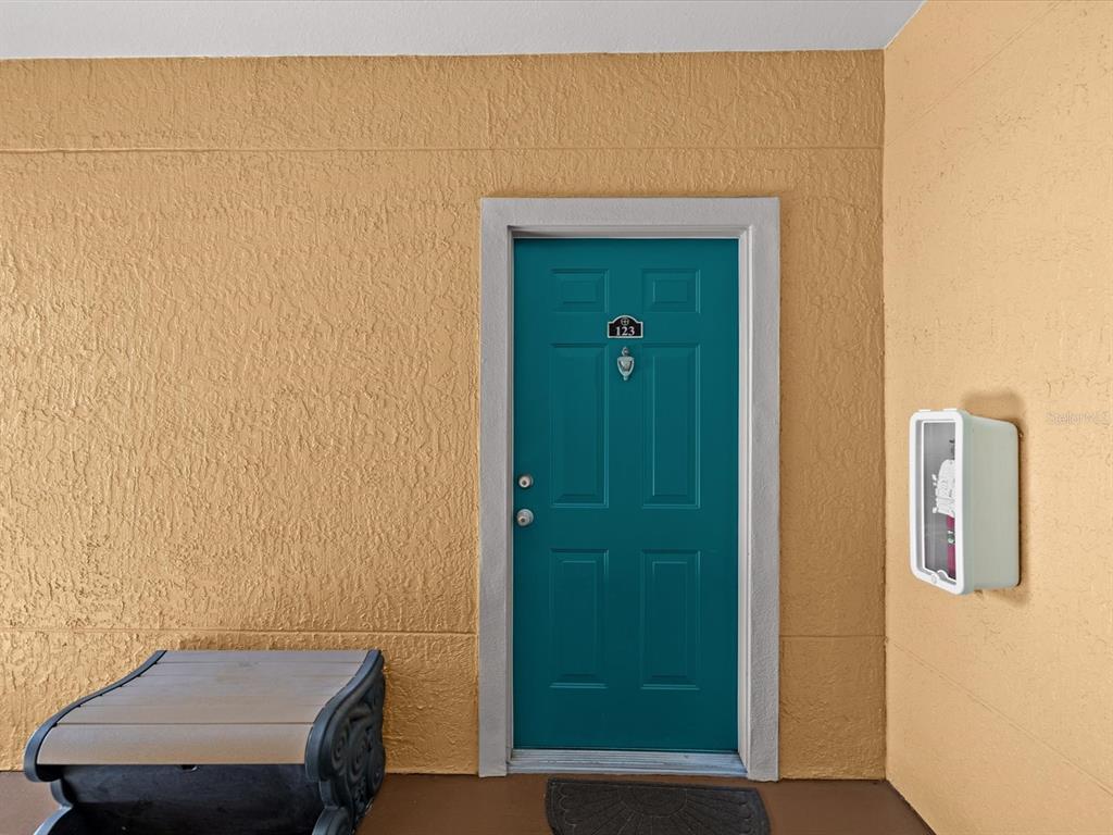 A teal front door with the number 123 is set in a textured yellow wall — 2705 VIA MURANO UNIT 123, CLEARWATER, FL