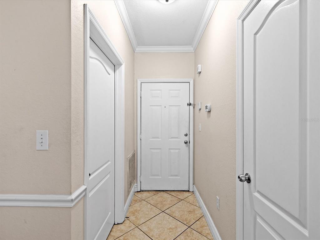 A narrow entryway features beige walls, white trim, tiled flooring, and three white doors — 2705 VIA MURANO UNIT 123, CLEARWATER, FL