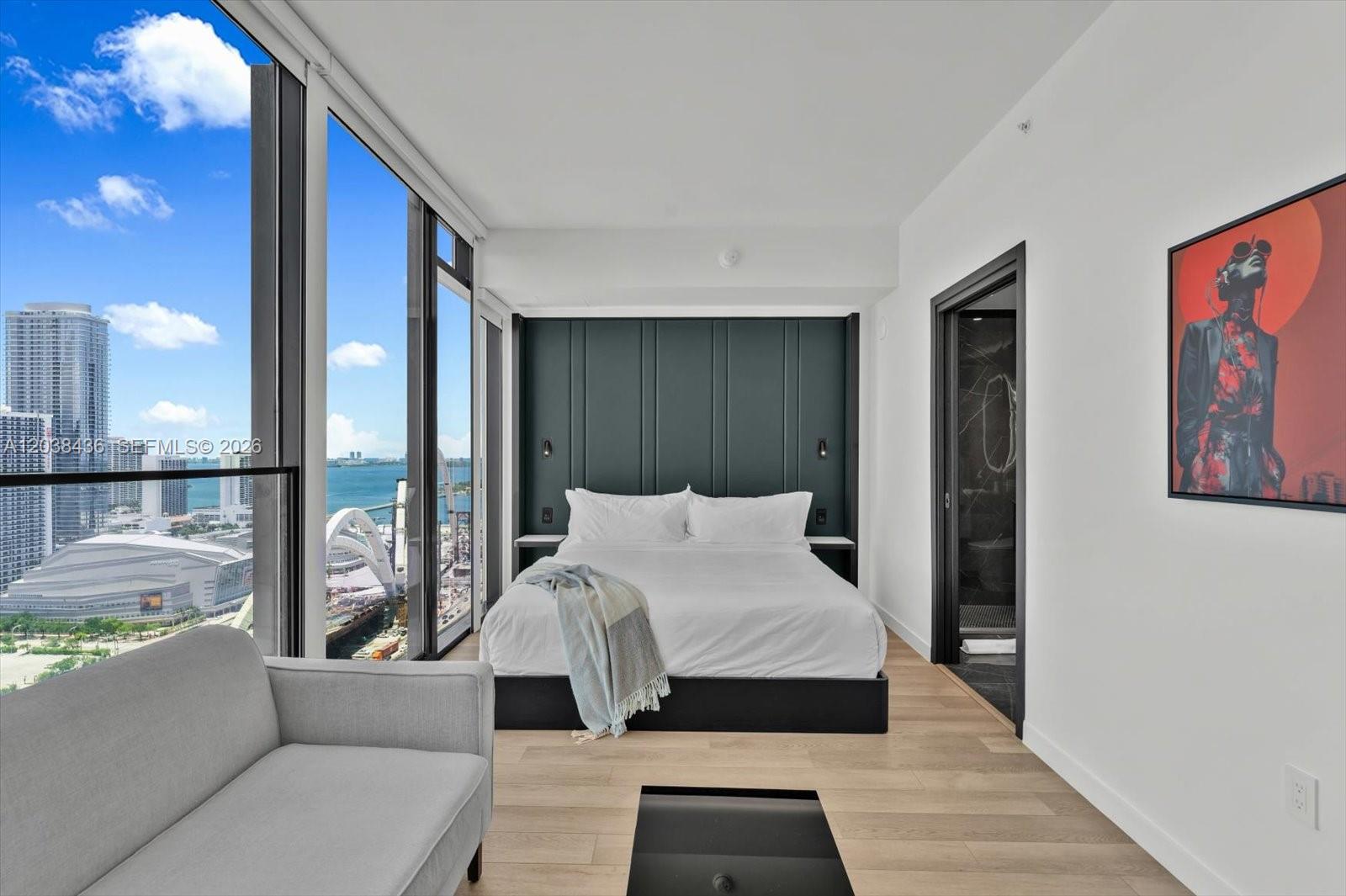 A modern bedroom features a dark paneled headboard, a white bed, and floor-to-ceiling city views — 20 NE 11th St # 3105, Miami FL 33132, MIAMI, FL