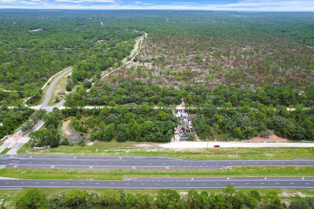 An aerial view shows a multi-lane highway bordering a wooded lot with a storage area — 17192 NICASIO JAY AVENUE, BROOKSVILLE, FL
