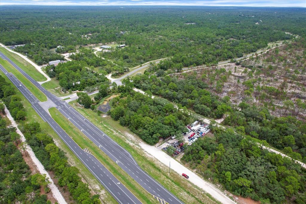 An aerial view shows a multi-lane highway bordering a wooded lot with a storage area — 17192 NICASIO JAY AVENUE, BROOKSVILLE, FL