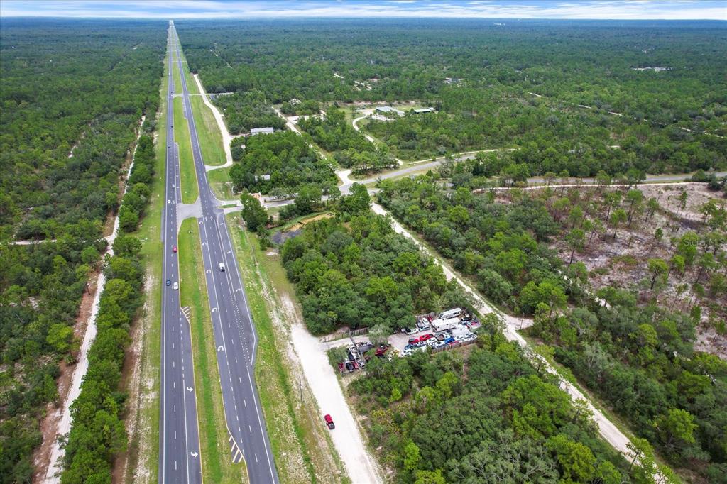 An aerial view shows a multi-lane highway running through a wooded area with a parking lot — 17192 NICASIO JAY AVENUE, BROOKSVILLE, FL