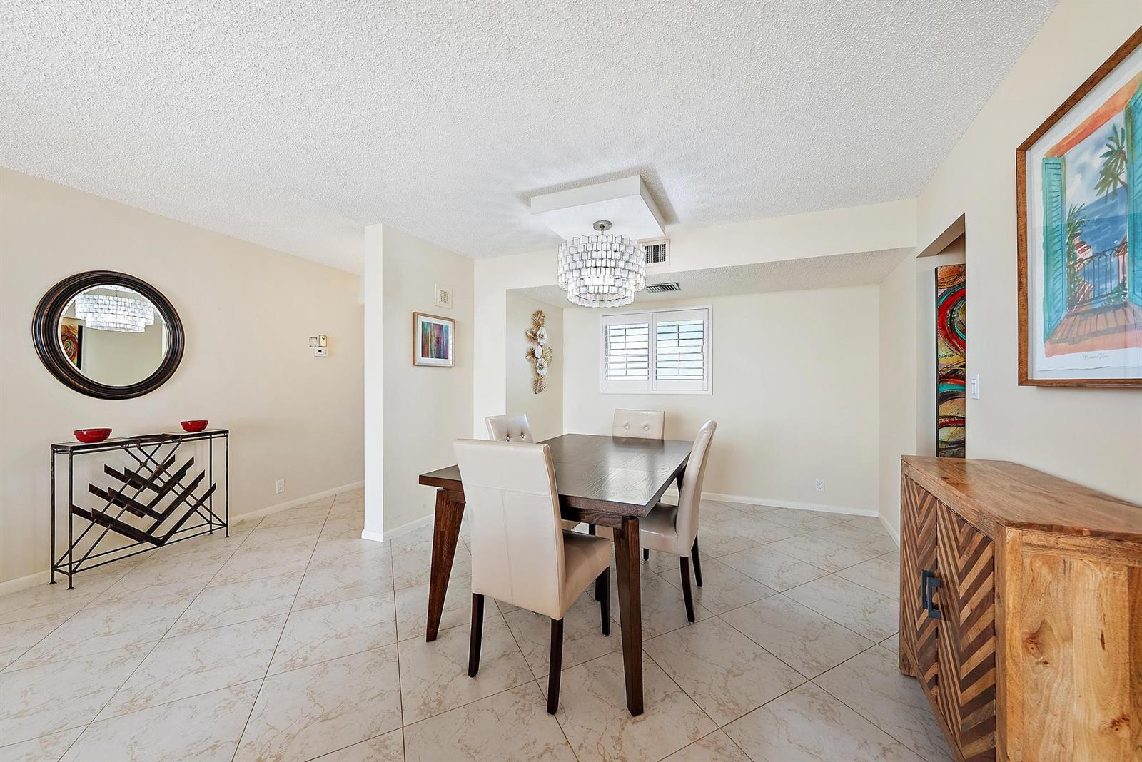 A dining room features a dark wood table, four beige chairs, and a crystal chandelier — 400 Ocean Trail Way # 707, Jupiter FL 33477, JUPITER, FL