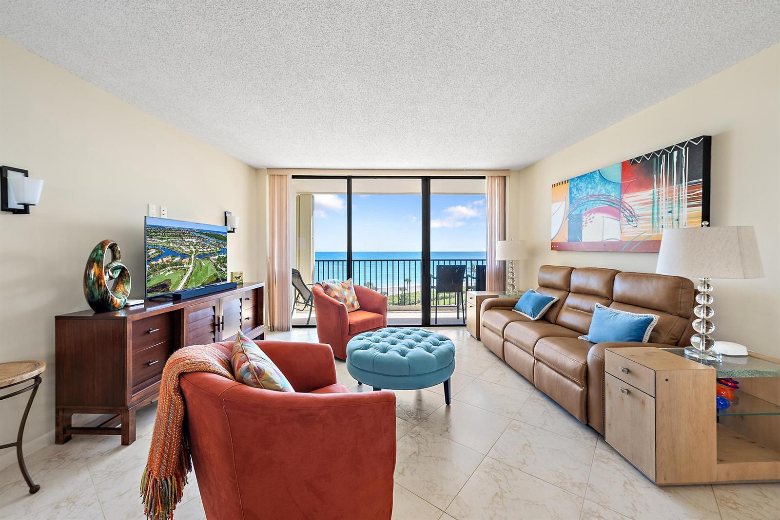 A living room features a brown leather sofa, two orange armchairs, and a blue ottoman — 400 Ocean Trail Way # 707, Jupiter FL 33477, JUPITER, FL