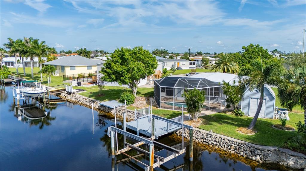 An aerial view shows a waterfront house with a screened pool, boat lift, and dock — 731 TANGERINE COURT, PUNTA GORDA, FL