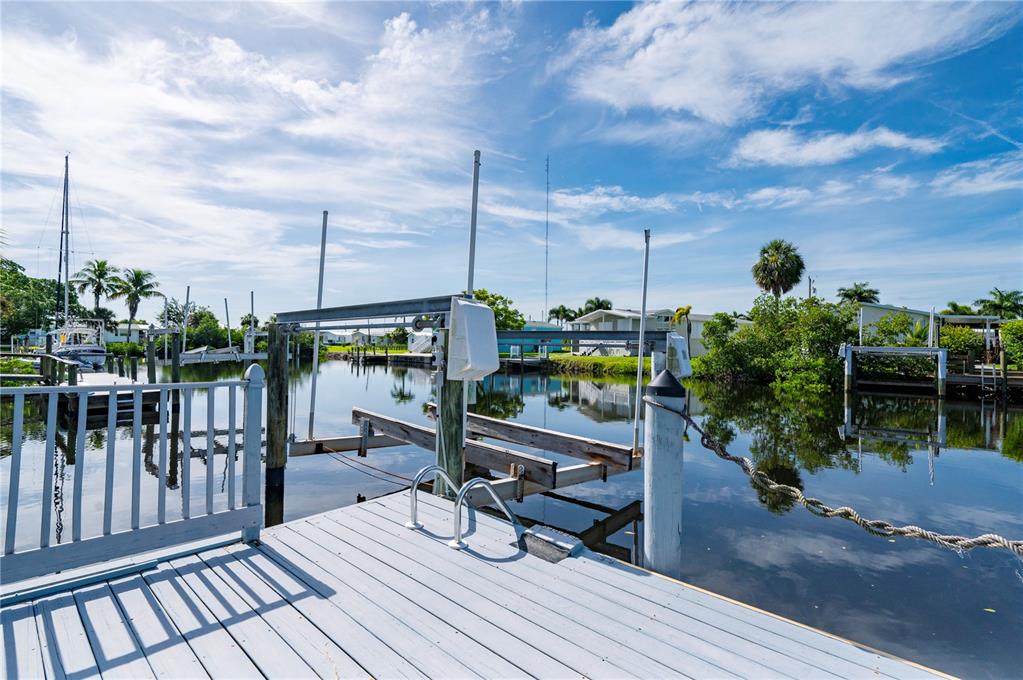 A wooden boat dock with a mechanical lift extends over a calm canal — 731 TANGERINE COURT, PUNTA GORDA, FL