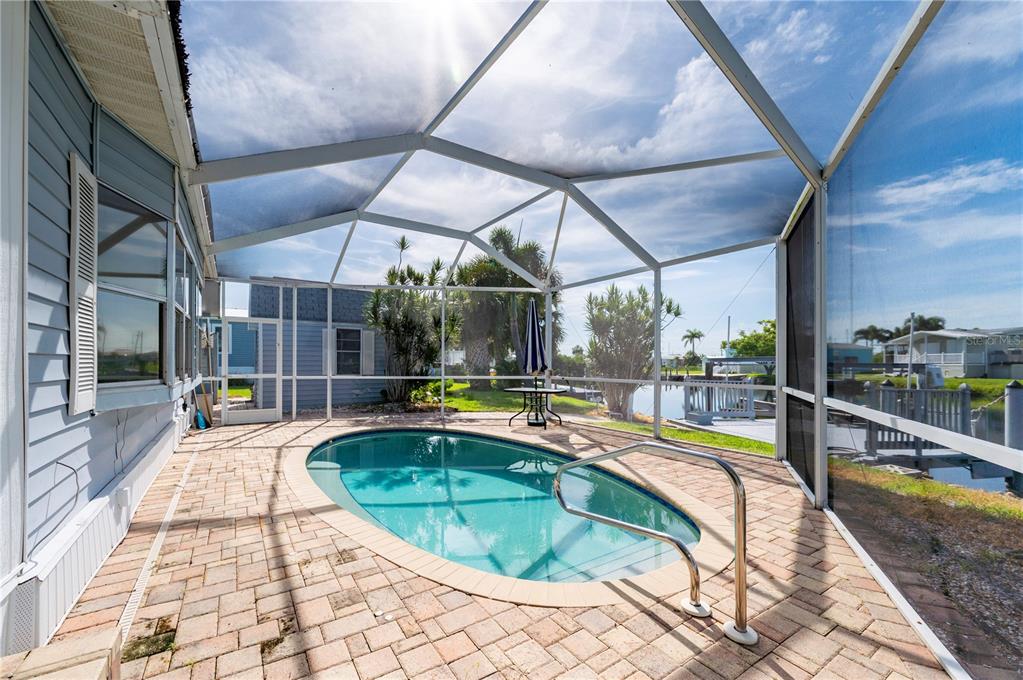 A screened-in pool patio features brick pavers, a small pool, and a view of water — 731 TANGERINE COURT, PUNTA GORDA, FL
