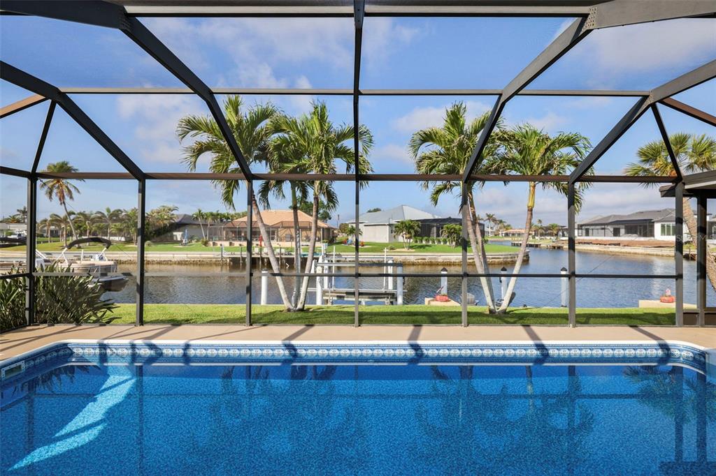A swimming pool sits inside a screened lanai overlooking a canal with palm trees and docks — 611 BAL HARBOR BOULEVARD, PUNTA GORDA, FL