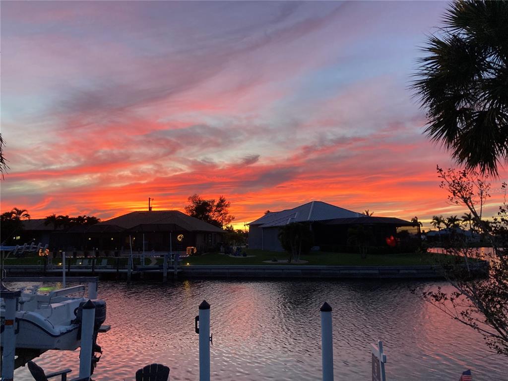A vibrant sunset glows over a canal with houses, boat docks, and palm trees — 611 BAL HARBOR BOULEVARD, PUNTA GORDA, FL