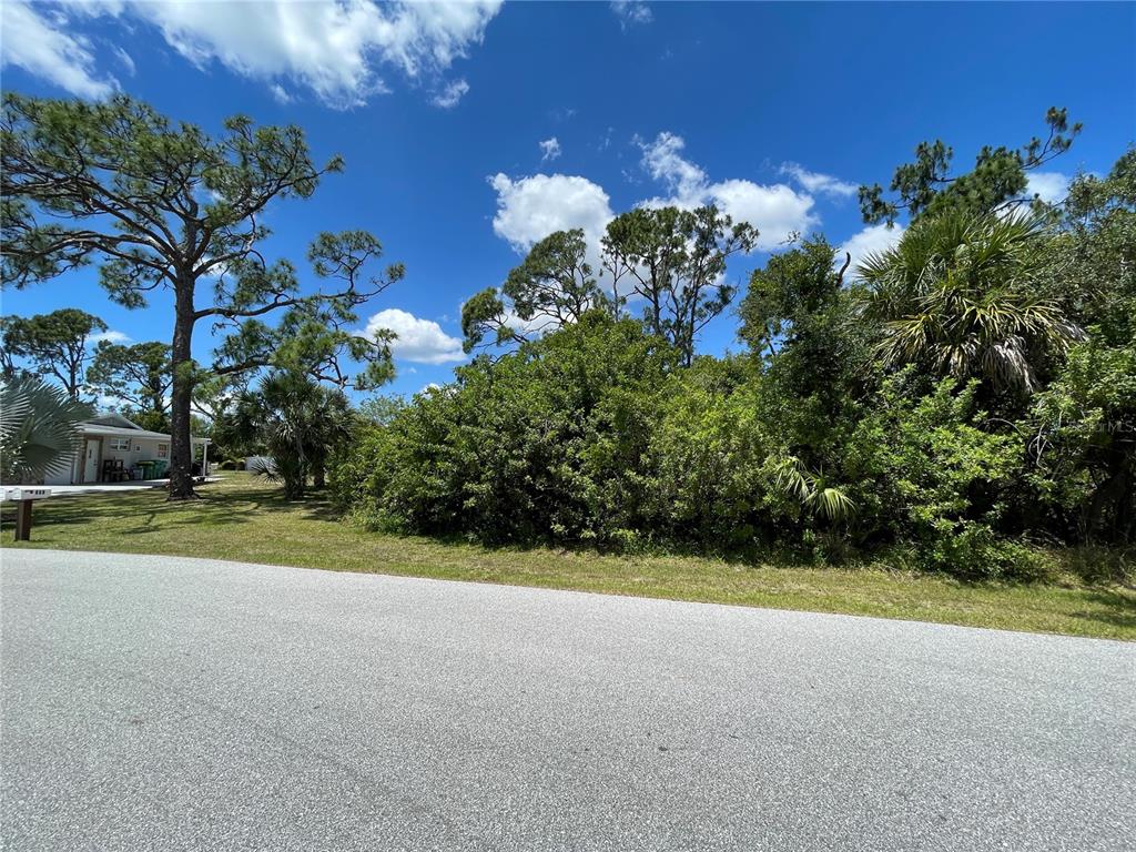 A paved road runs in front of a vacant, wooded lot with mature pine trees — 468 KELLSTADT STREET NW, PORT CHARLOTTE, FL