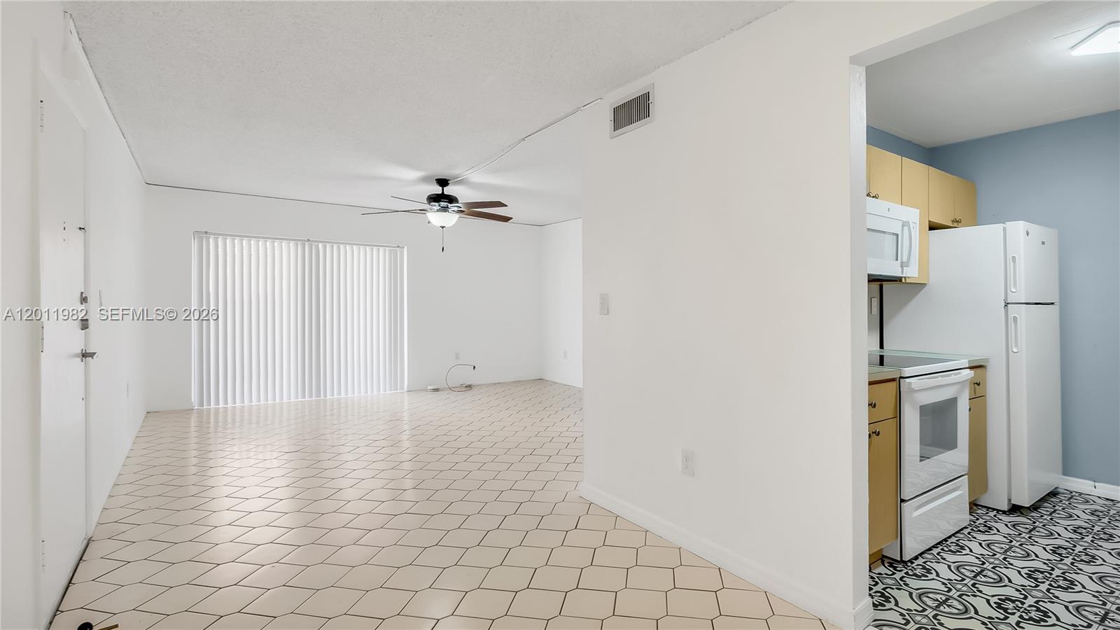 An open living area with tile flooring leads to a kitchen with white appliances — 7231 Miami Lakes Dr # C5, Miami Lakes FL 33014, MIAMI LAKES, FL