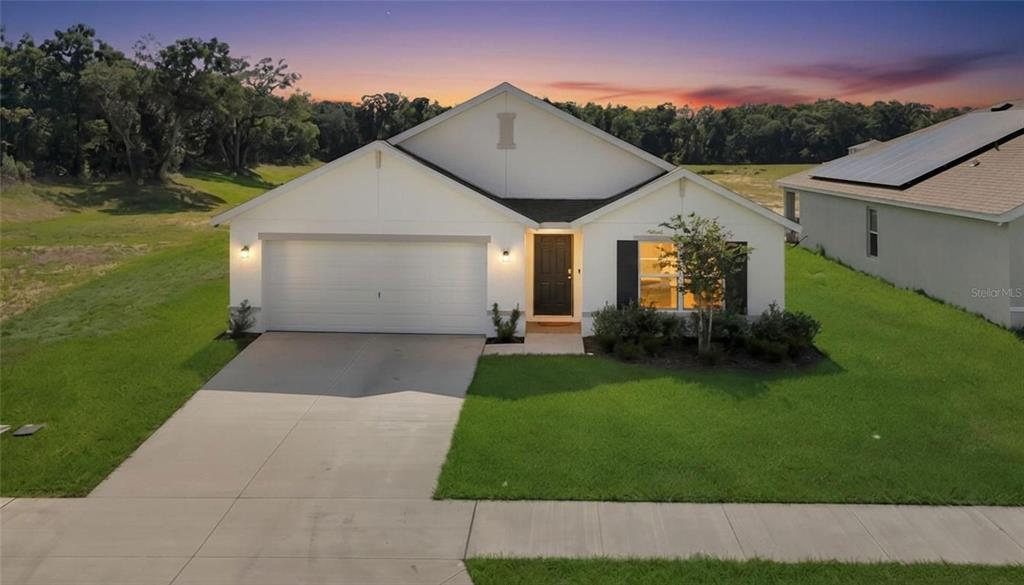 A single-story house with a white exterior, two-car garage, and a front lawn at dusk — 11446 SE 72ND AVENUE, BELLEVIEW, FL