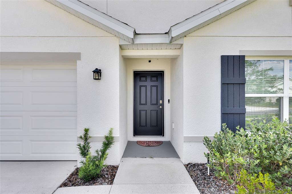 A white house exterior features a dark front door, a garage, and a small garden — 11446 SE 72ND AVENUE, BELLEVIEW, FL