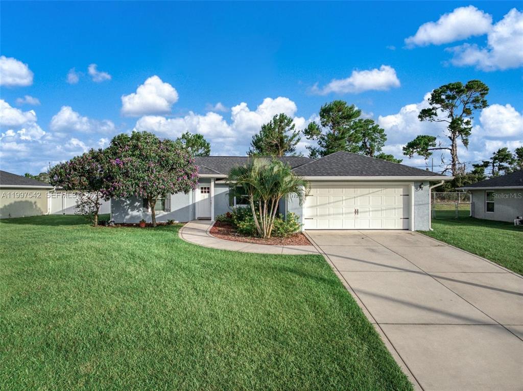 A single-story house with a white garage door, a paved walkway, and a large lawn — 112 NE BIMINI STREET NE, LAKE PLACID, FL