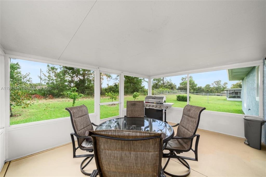 A screened-in patio features a glass-top dining table, four chairs, and a gas grill — 112 NE BIMINI STREET NE, LAKE PLACID, FL
