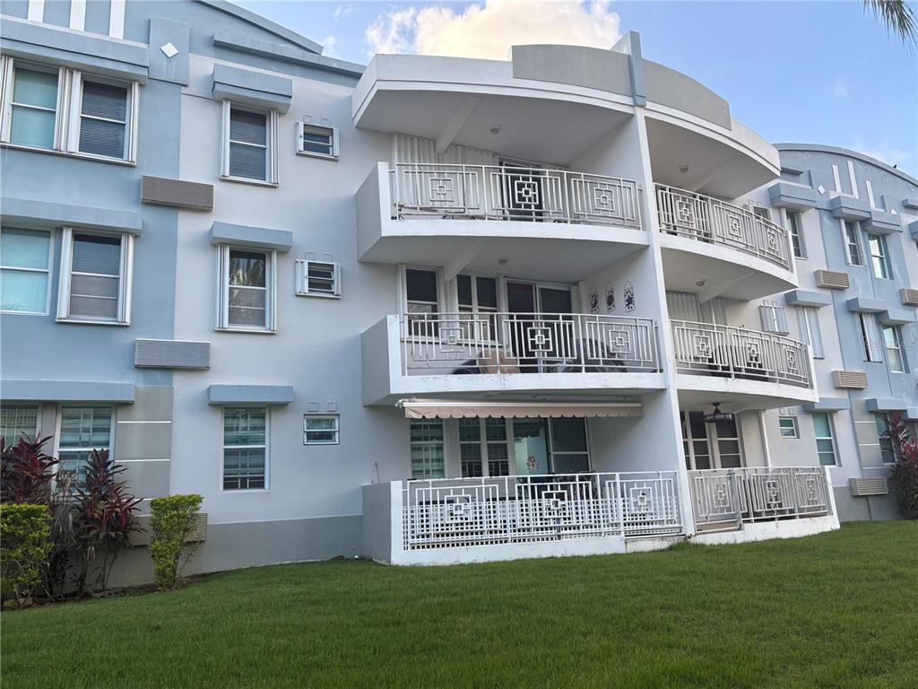 A three-story apartment building features white stucco walls, balconies with decorative railings, and green landscaping — 1502 OCEAN POINT UNIT 1, LOIZA, PR