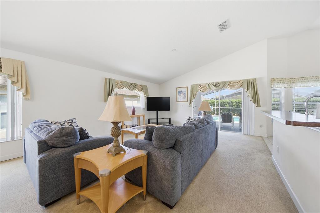 A living room features gray sofas, a wooden side table, and sliding doors to a pool — 723 OLD BRIDGE CIRCLE, DAVENPORT, FL