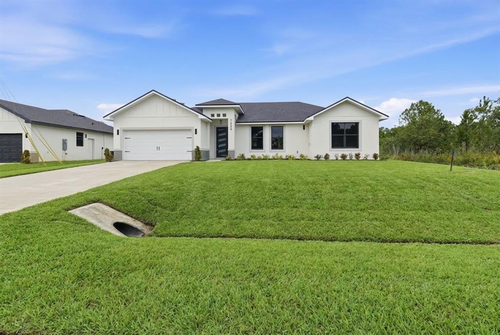 A single-story white house with a dark roof and a two-car garage sits on grass — 7224 GRANADA BOULEVARD, SEBRING, FL