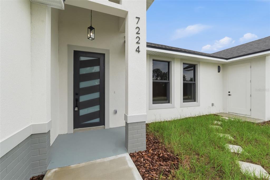 A modern home entrance features a dark front door with glass panels and gray brick accents — 7224 GRANADA BOULEVARD, SEBRING, FL