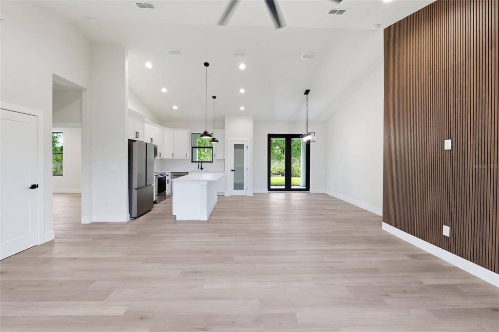 An open-concept kitchen and living area features light wood flooring and a wood-slat accent wall — 7224 GRANADA BOULEVARD, SEBRING, FL