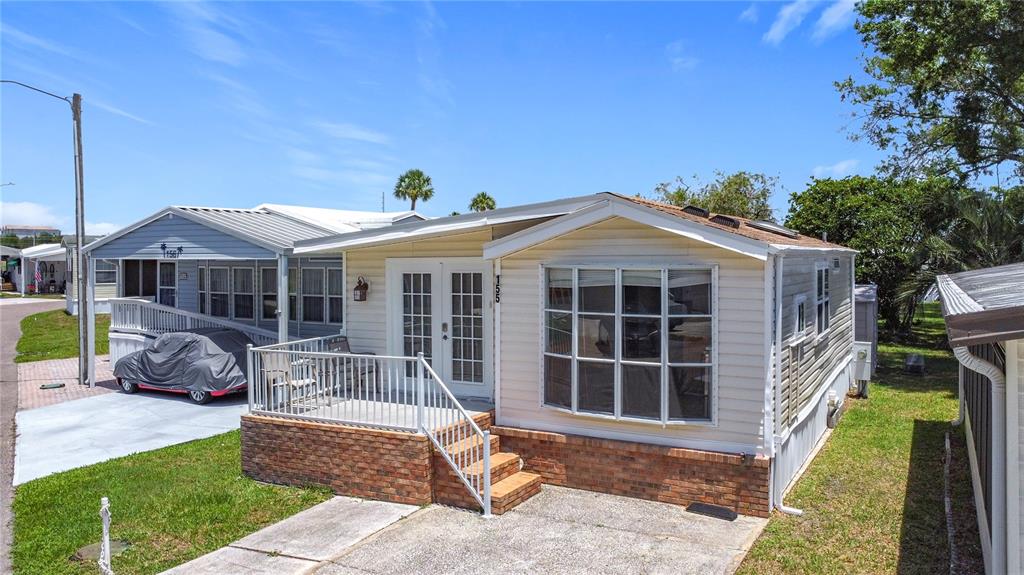 A light-colored manufactured home features a brick-based front porch, a bay window, and a driveway — 9000 US HIGHWAY 192 UNIT 155, CLERMONT, FL